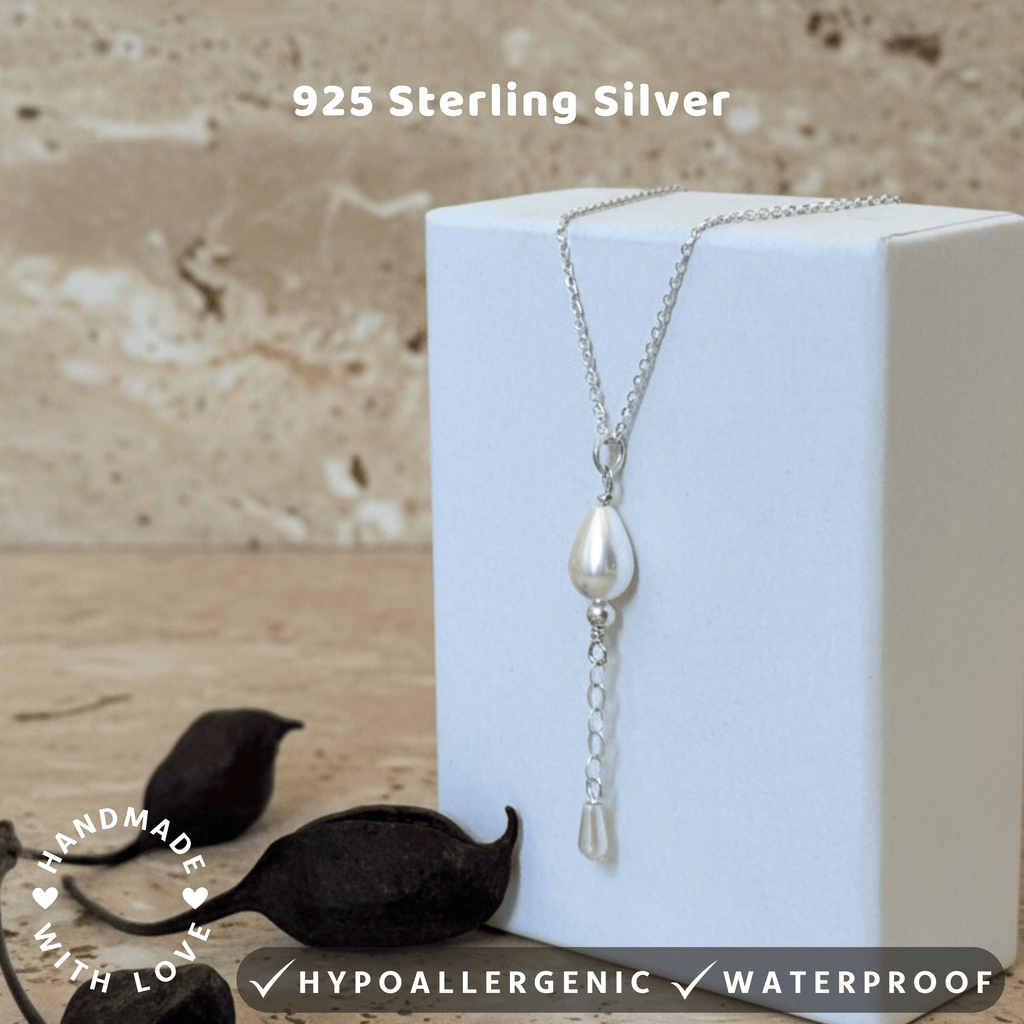 Silver necklace with a pearl pendant with a drop 20mm chain and bead on a white box against a textured beige backgroun