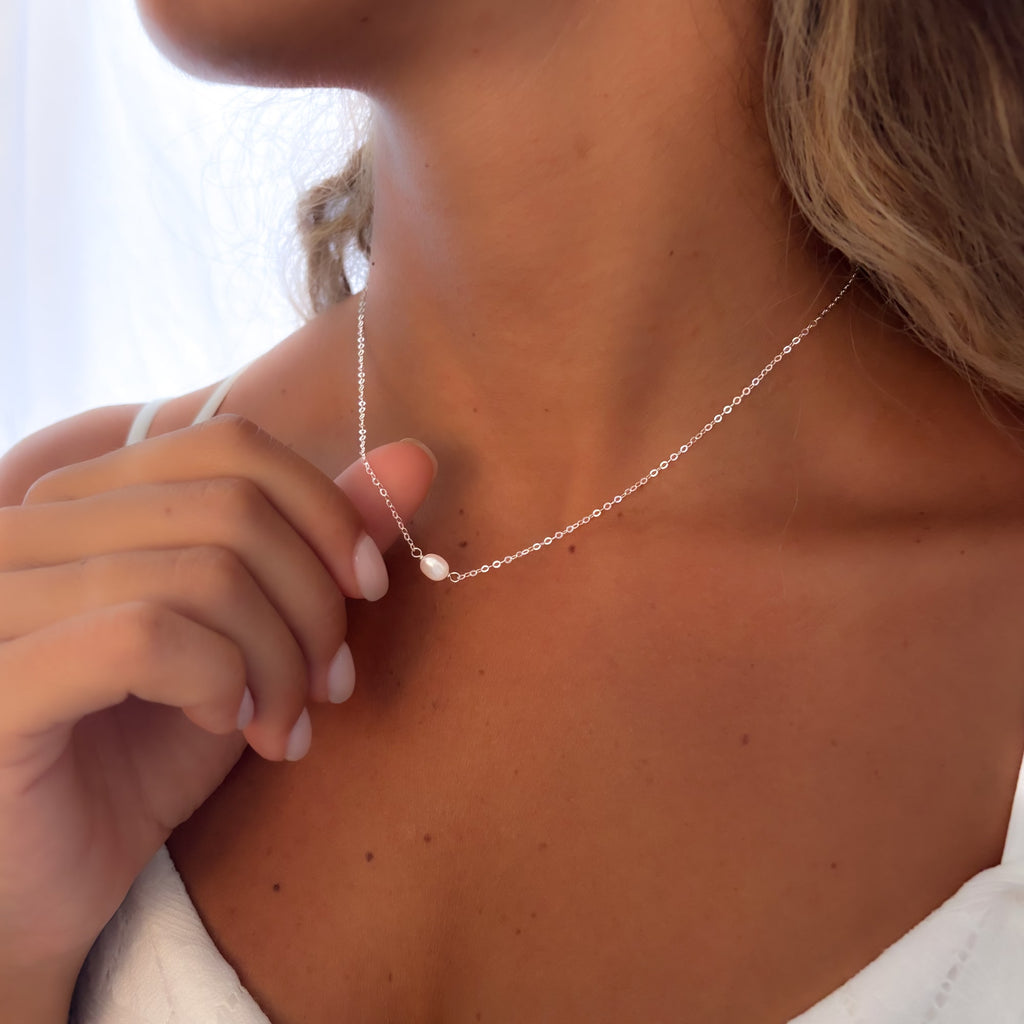 Close-up of a woman wearing a delicate silver necklace with a small pearl charm