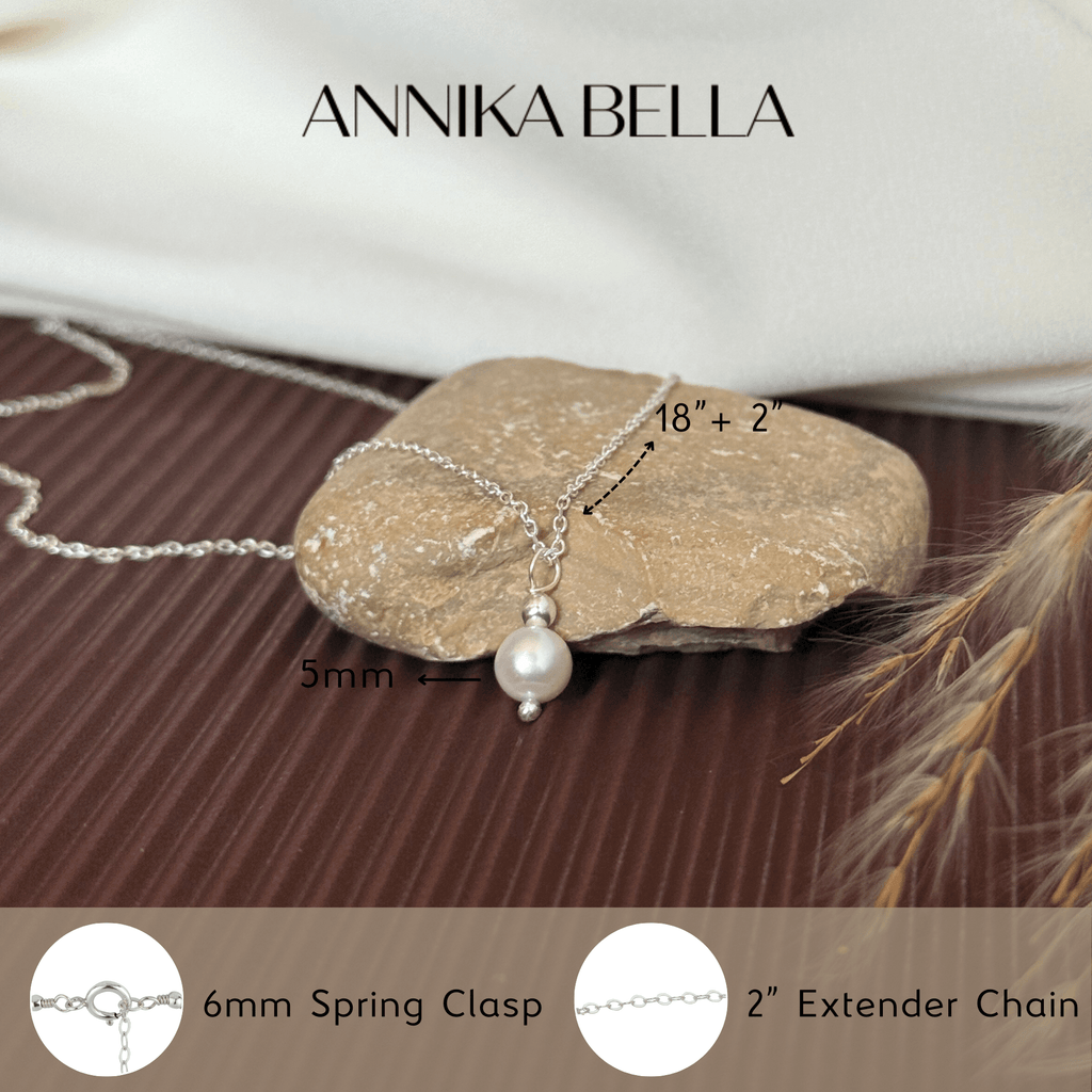 Silver necklace with pearl pendant on a rock, featuring 'AnniKA BELLA' branding.