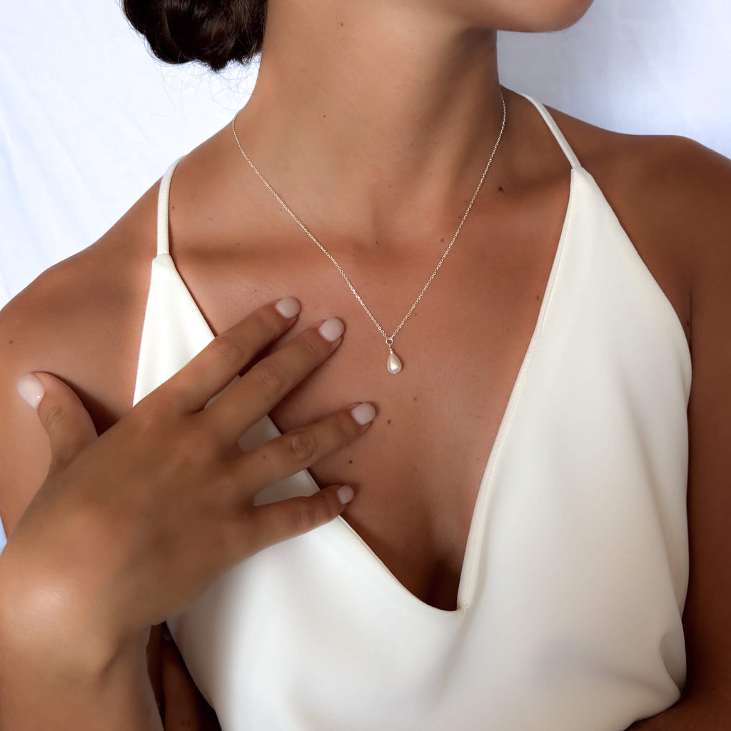Woman wearing a delicate necklace with a pearl pendant on a white background