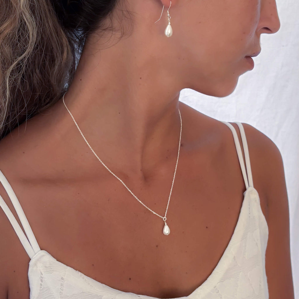 Woman wearing a delicate necklace and earrings set on a plain background
