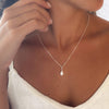 Woman wearing a delicate necklace with a teardrop pearl pendant.