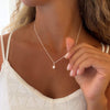 Woman wearing a delicate necklace with a small pearl pendant, close-up of the necklace and hand holding the dainty silver chain.