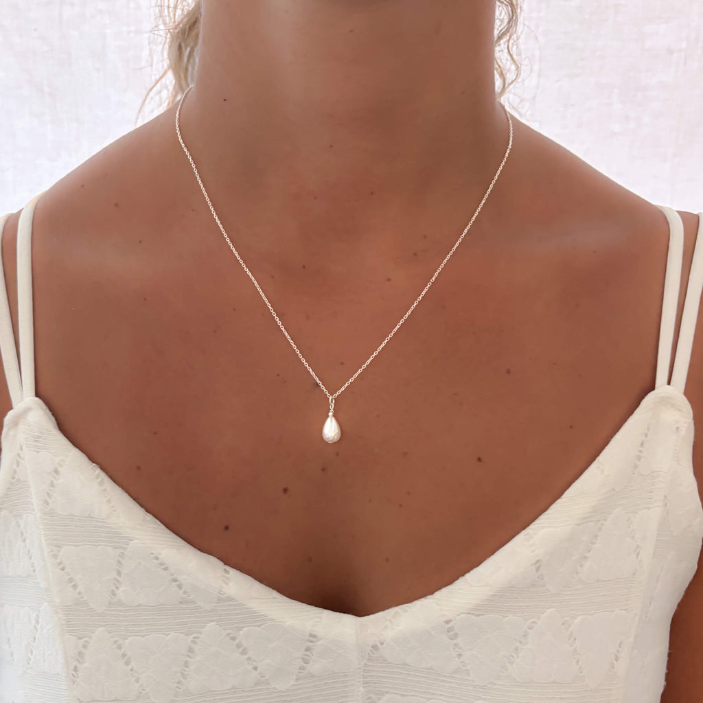 Pearl silver necklace worn by a woman with a white tank top on a white background