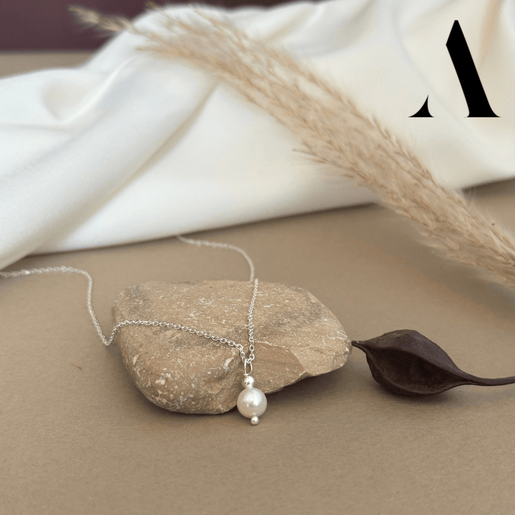 Silver necklace with a pearl charm on a stone surface with a leaf and fabric in the background