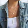 stack of silver necklaces. a long feather, a textured sparkly disc necklace, a turquoise and silver chain and a snake choker