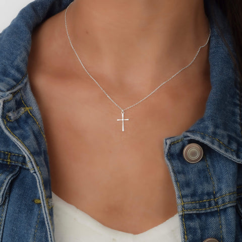 Silver cross pendant necklace on a  woman wearing a jean jacket